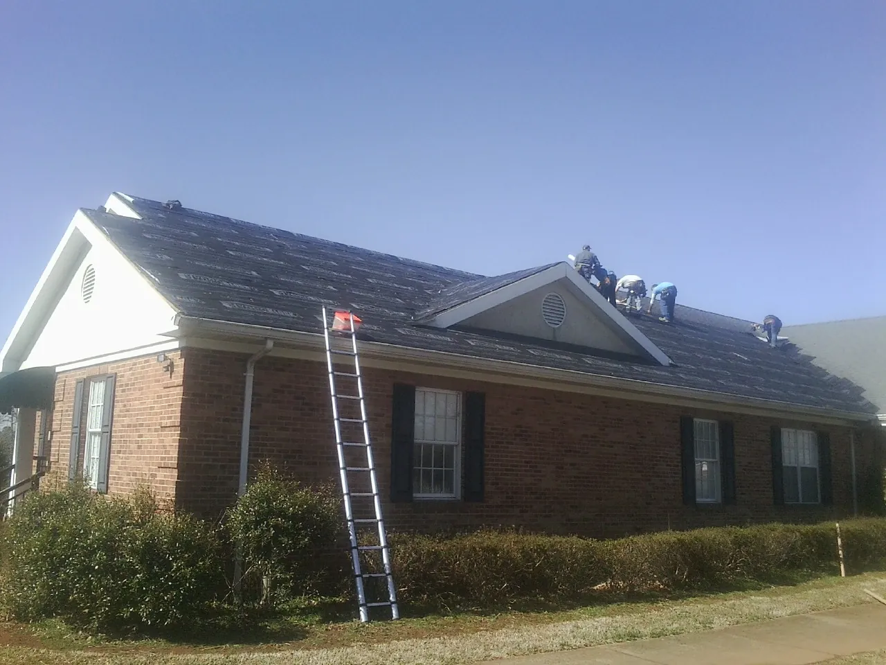 Crew tearing shingles off a brick ranch roof with a ladder set — Emergency Roof Repair work by our crew in York