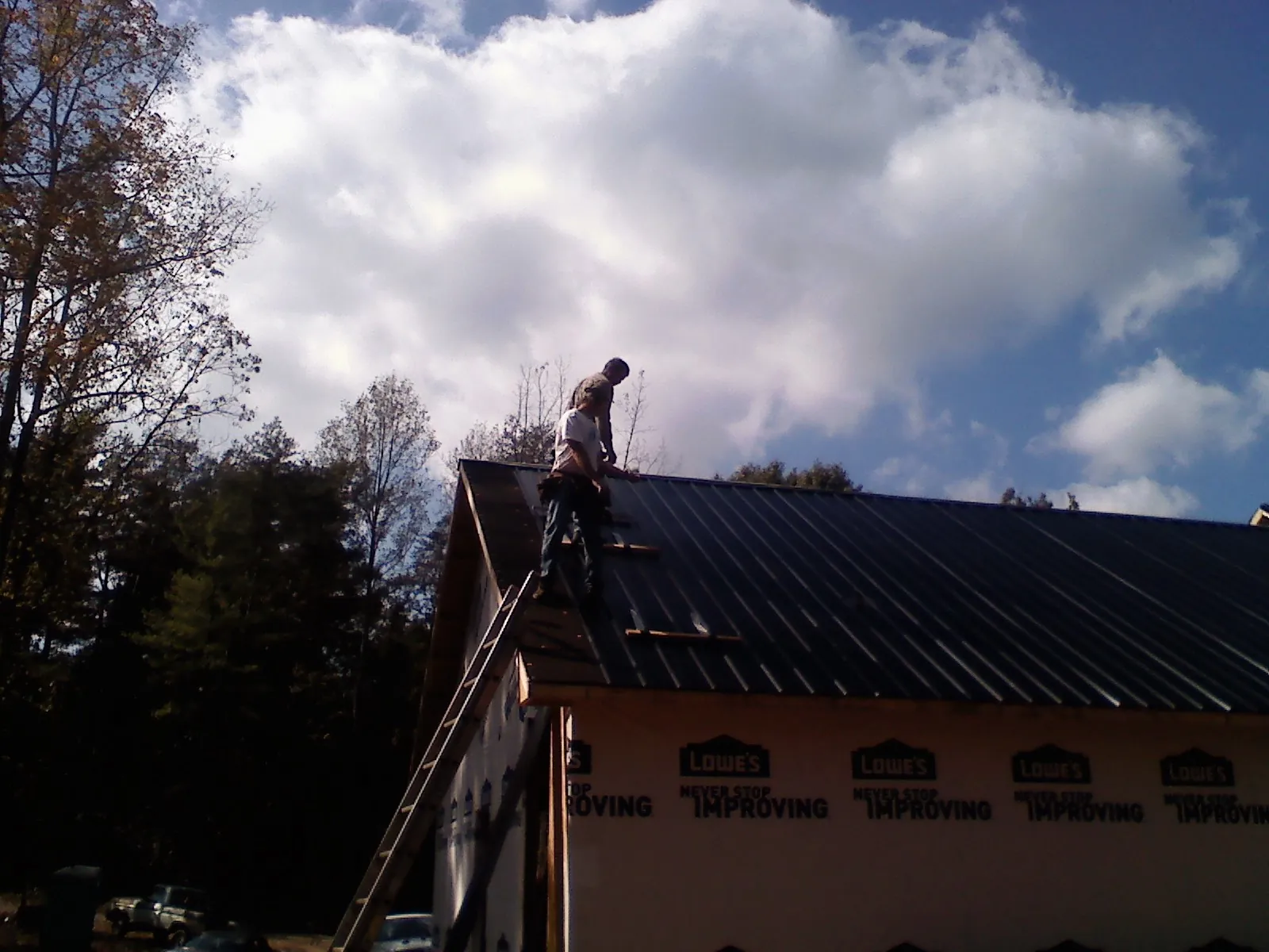 Roofer fastening dark metal panels high against a cloudy sky, from a Roof Inspection job in York